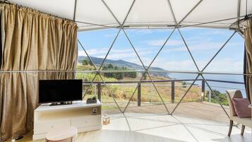 Una habitación con un ventanal grande, televisión, una mesita y una silla.