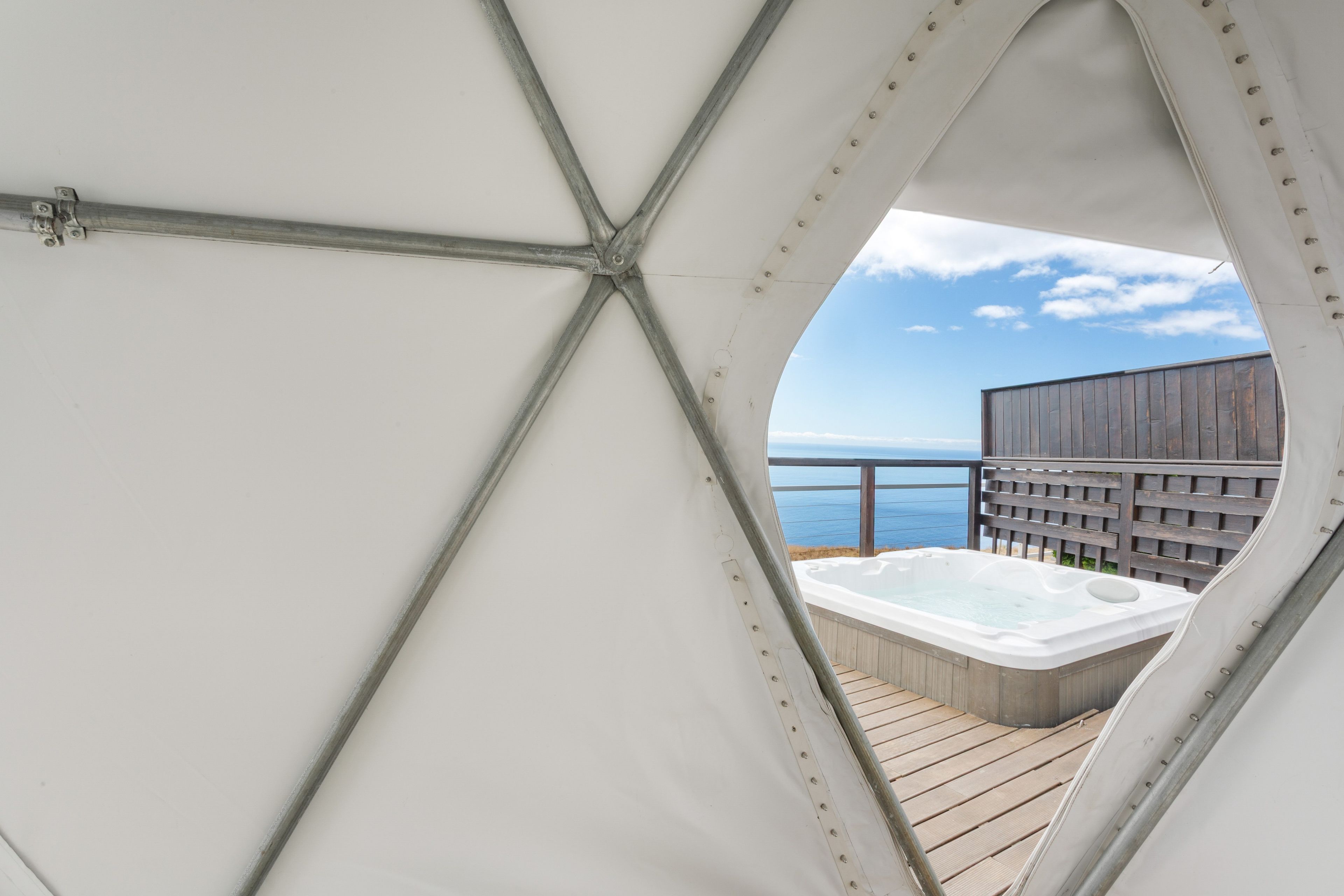 Vue de l’intérieur d’une structure ressemblant à une tente, dotée d’une terrasse en bois et d’un bain à remous.