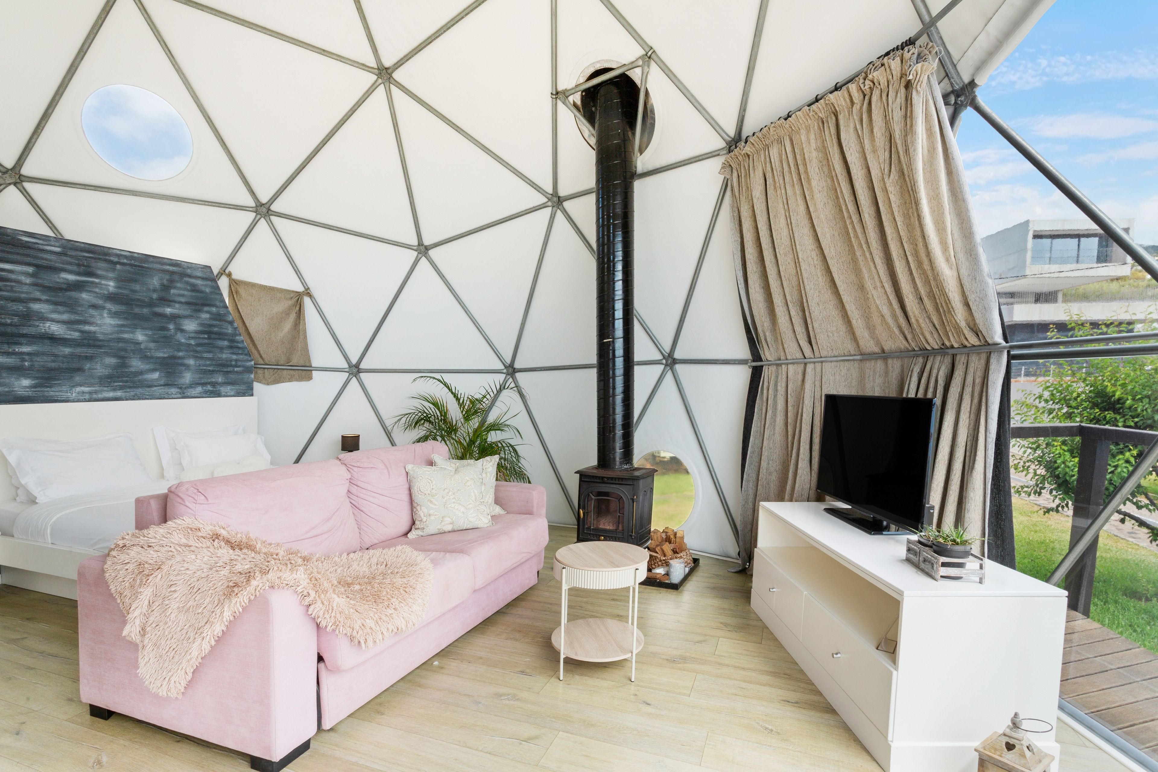 A cozy living room with a pink sofa, a small round table, a TV, and a wood-burning stove.