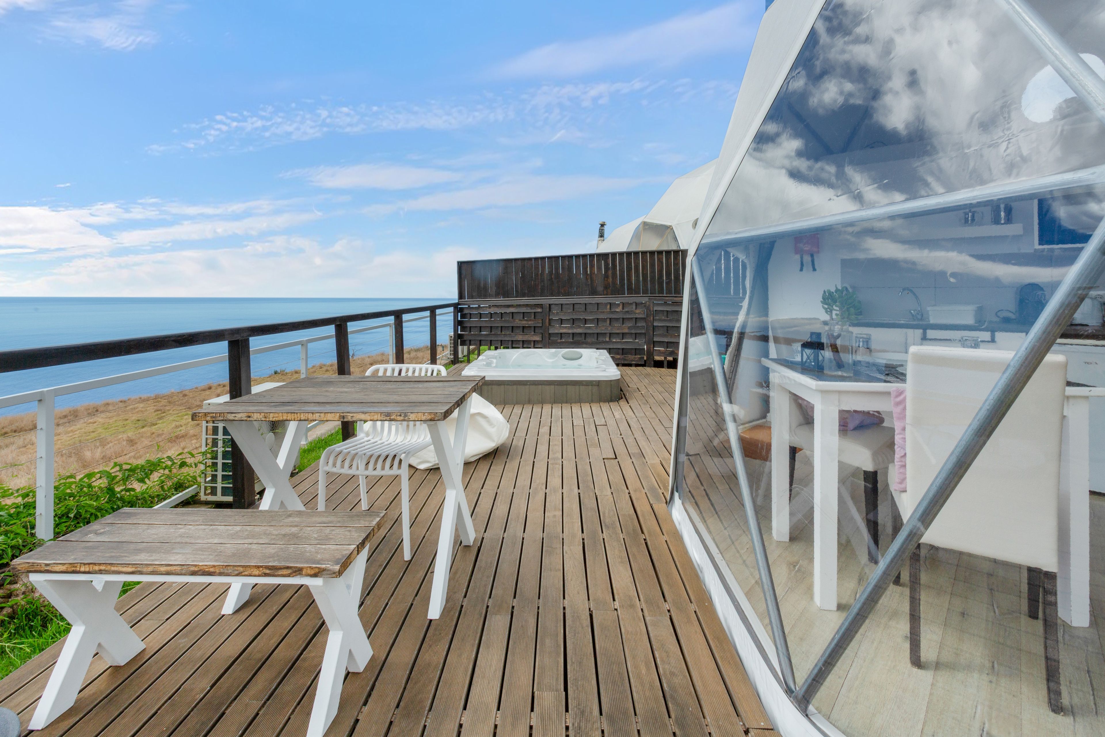 A wooden deck with a table and chairs, overlooking a beach.