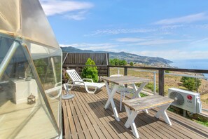 A deck with outdoor furniture, a view of the sea, and a mountainous landscape in the background.