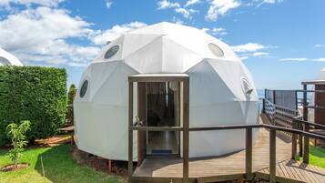Una estructura de domo geodésico con una terraza de madera y una puerta que da al interior.