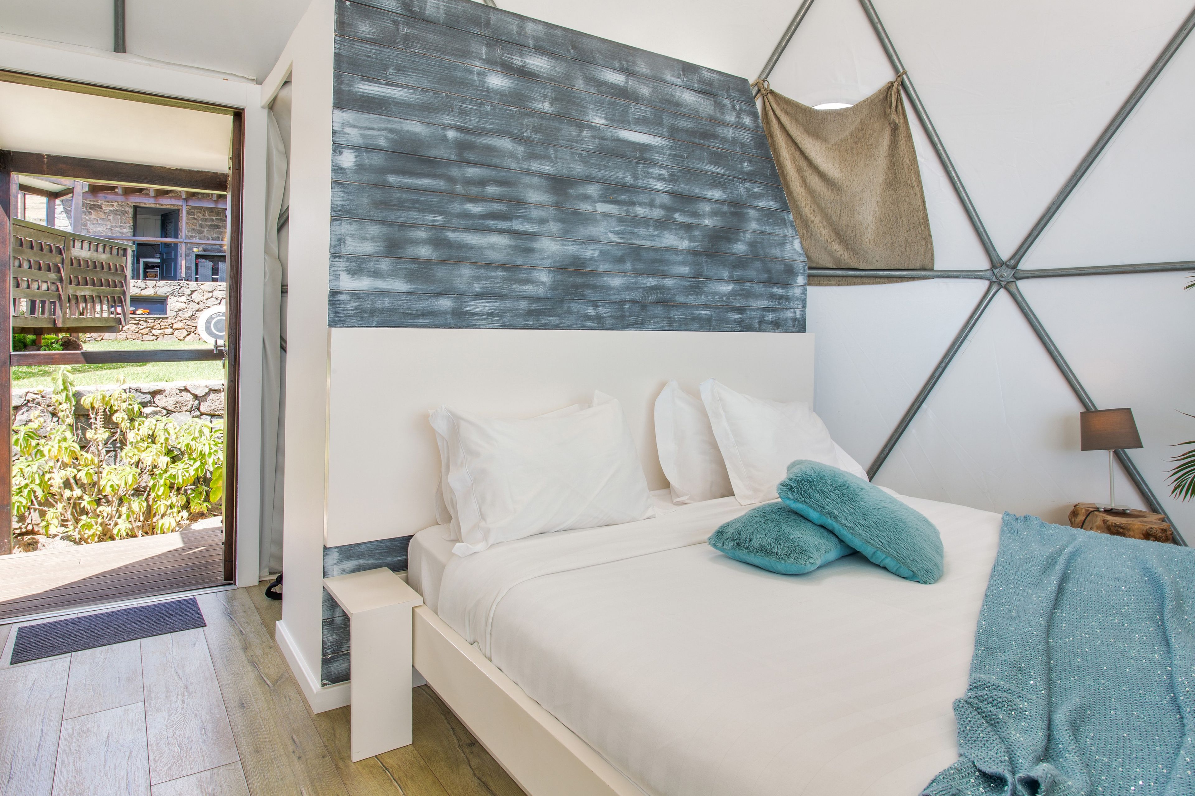 Un dormitorio con cama, almohadas, una toalla azul y vista a un jardín a través de una puerta abierta.