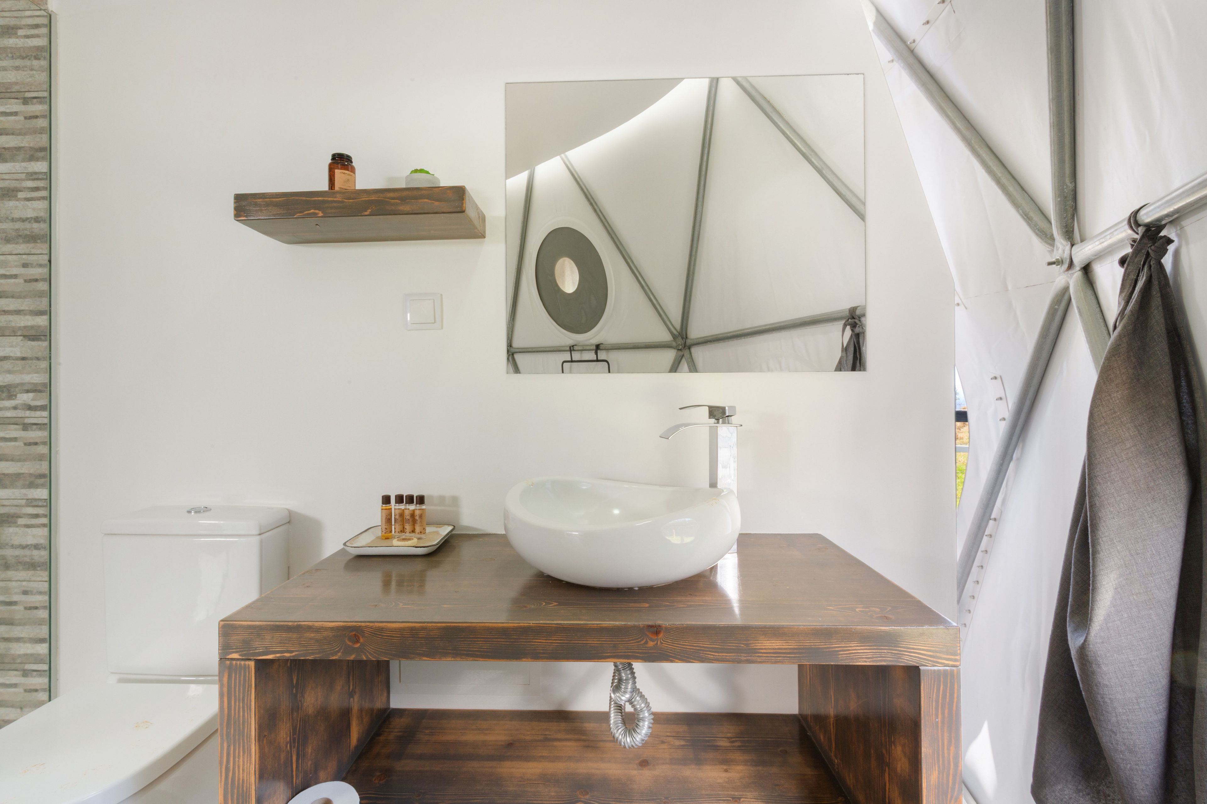 Ein Badezimmer mit einem Holz-Waschtisch, einem weißen Waschbecken, einem Spiegel und einem Handtuch, das an einer Metallstange hängt.