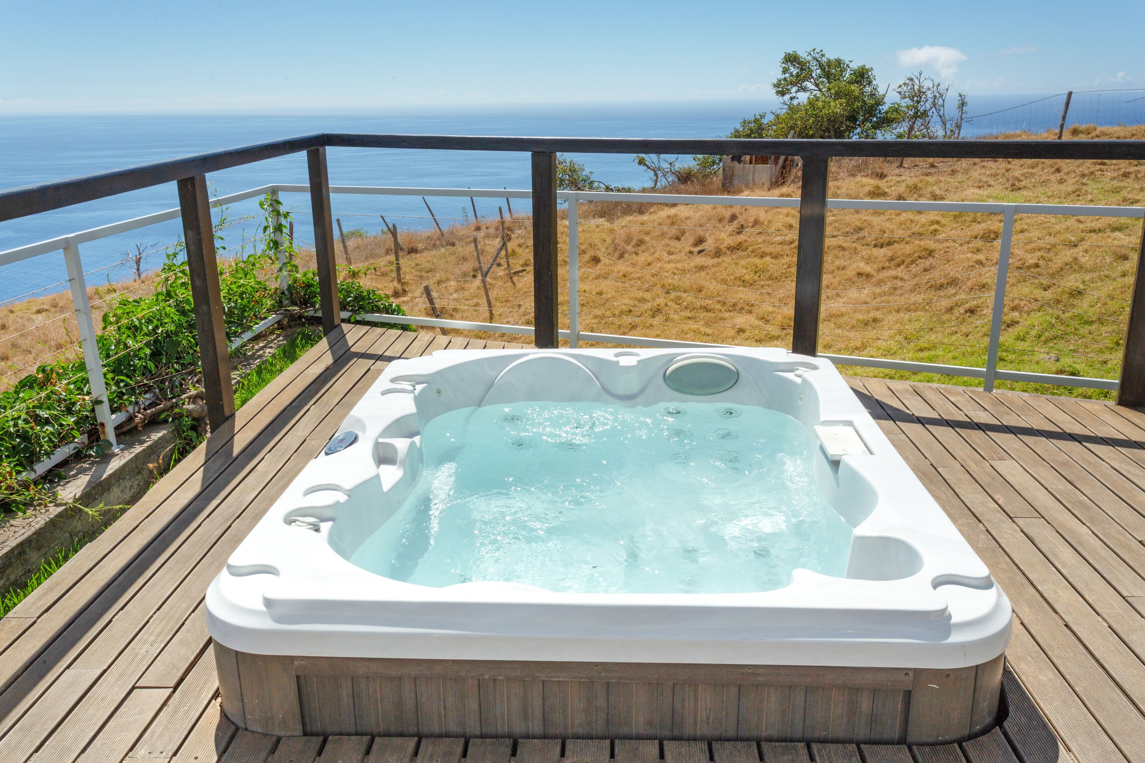 A hot tub on a wooden deck with a view of the ocean.