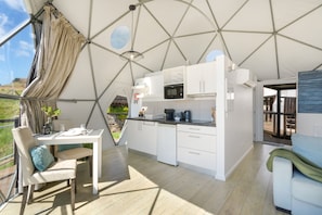 Une cuisine moderne avec des meubles blancs, un coin repas comprenant une table et des chaises, et une vue sur l’extérieur grâce à une grande fenêtre.