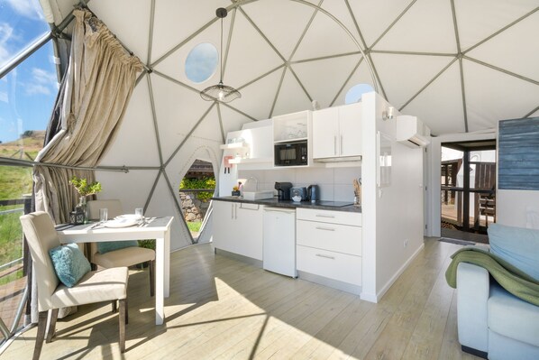 A modern kitchen with white cabinetry, a dining area with a table and chairs, and a view of the outdoors through a large window.