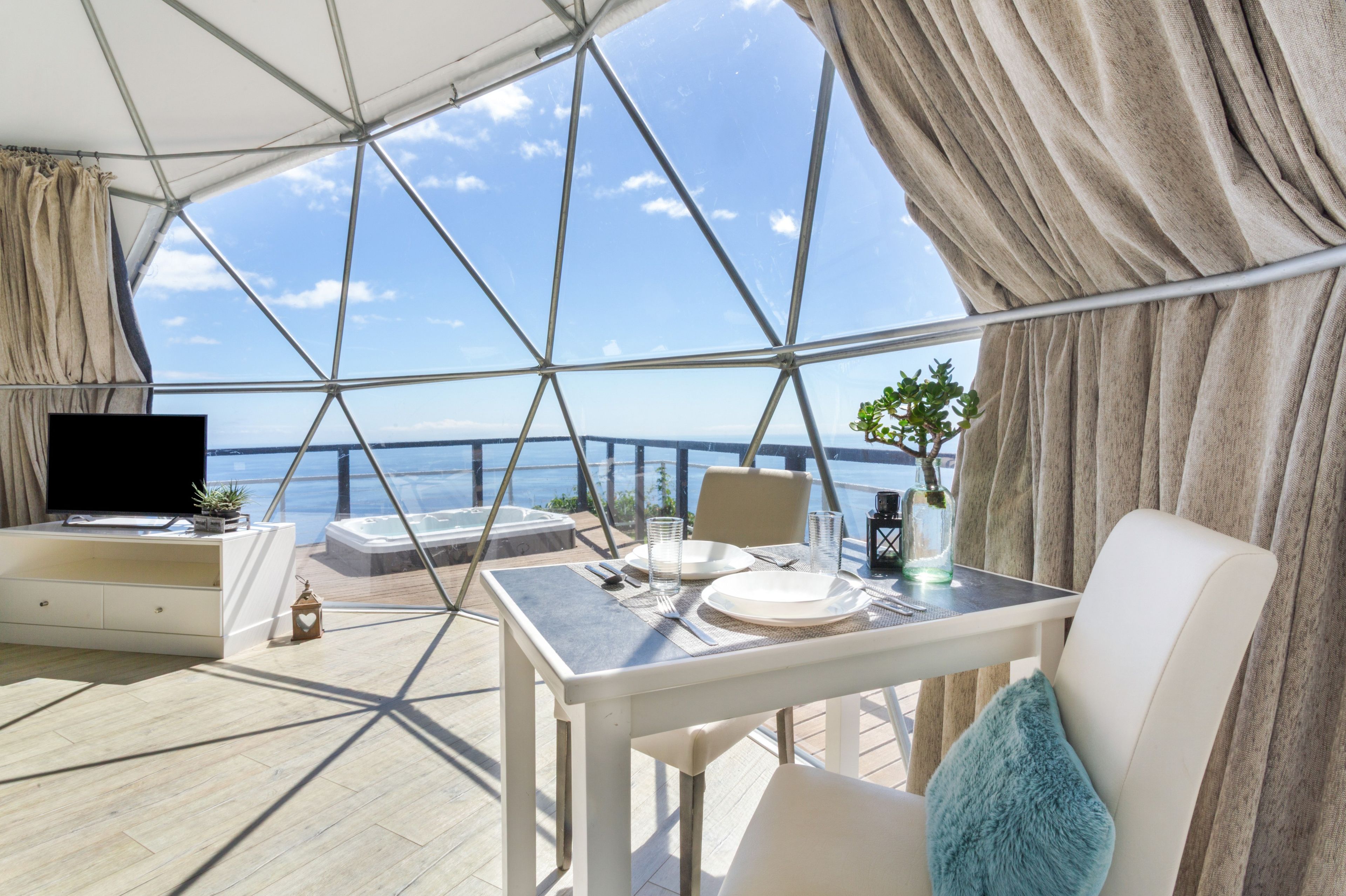 Una terraza con mesa lista para comer, un sofá, un televisor y vista al mar.
