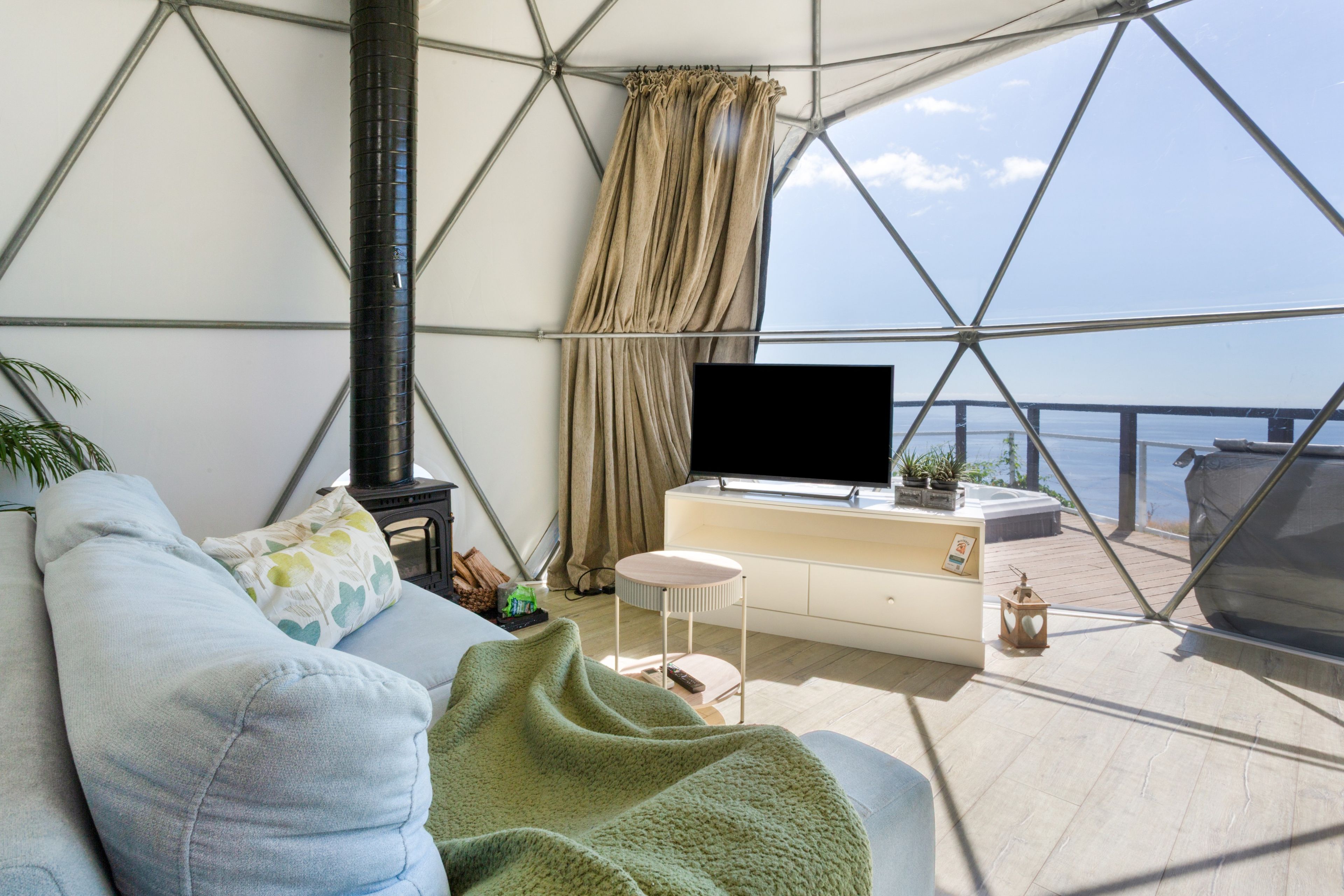 Un salon moderne avec un canapé, un téléviseur à écran plat et une vue sur la mer, visible à travers une grande fenêtre.