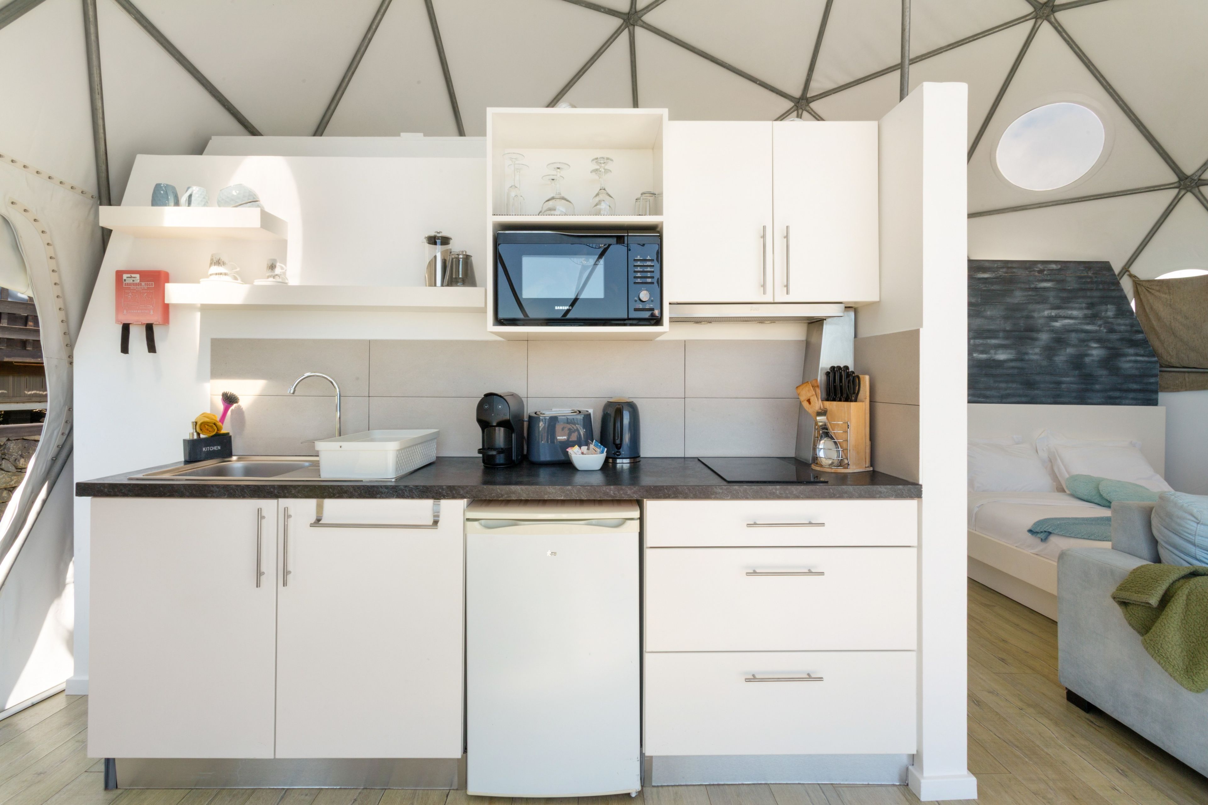 Een kleine keuken met witte kastjes, een ingebouwde magnetron en een koffiezetapparaat.