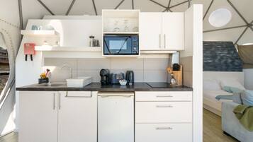 Een kleine keuken met witte kastjes, een ingebouwde magnetron en een koffiezetapparaat.