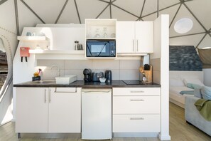 Une cuisine compacte avec des meubles blancs, un four à micro-ondes encastré et une machine à café.