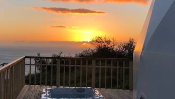Een houten terras met een jacuzzi en uitzicht op de ondergaande zon boven de oceaan.