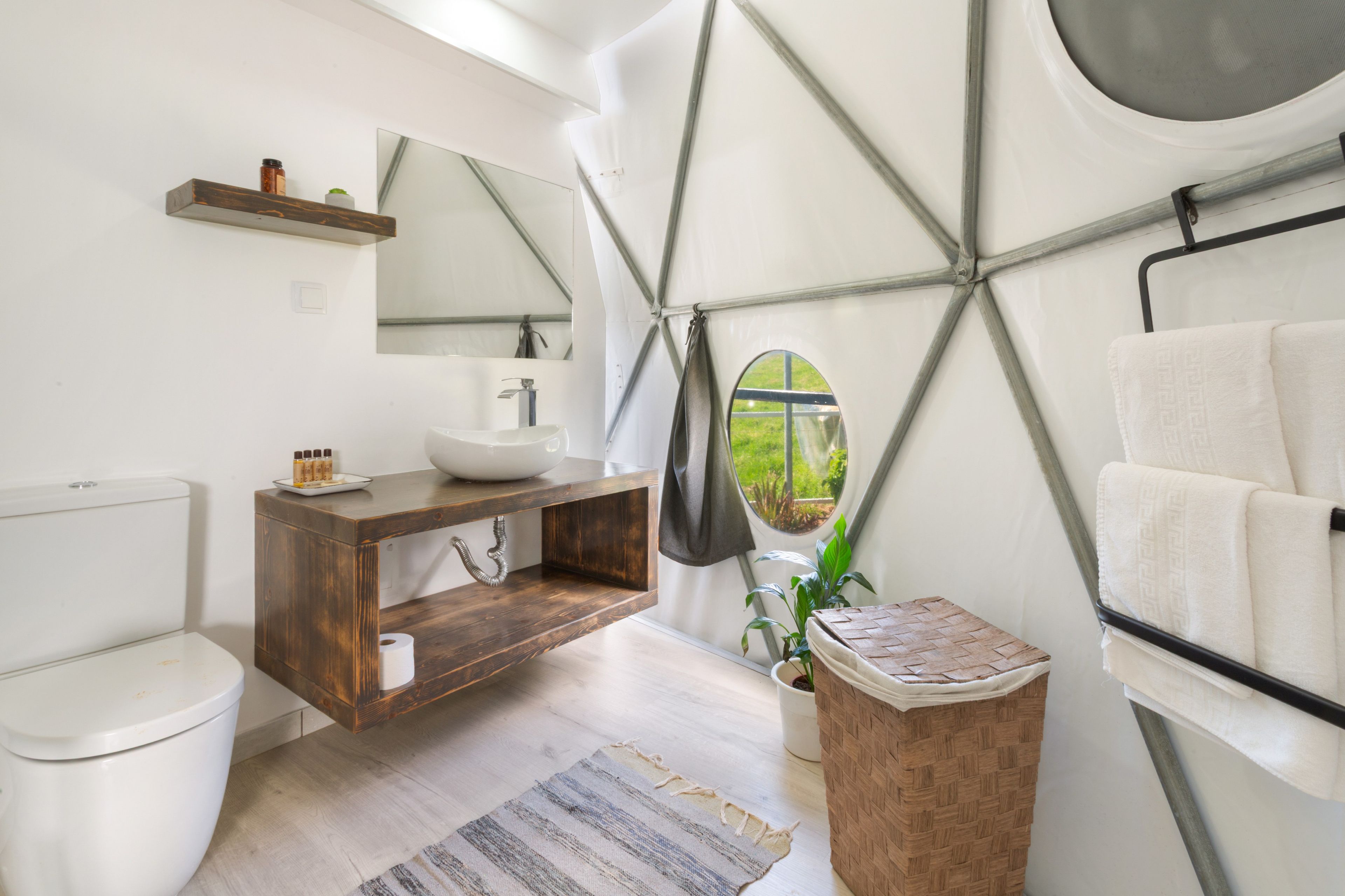 A modern bathroom with a wooden vanity, a white sink, a large mirror, and a round window.