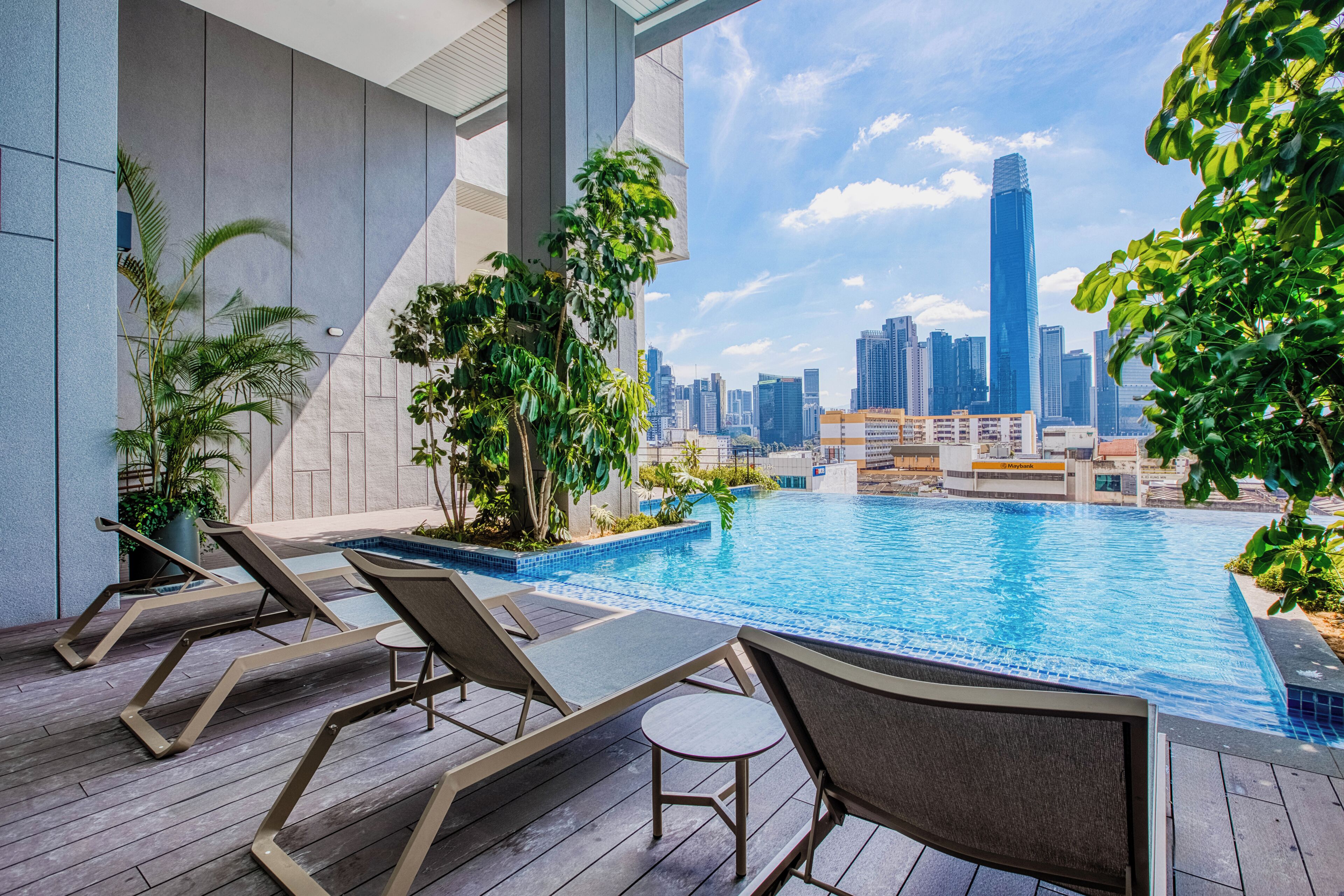 A rooftop pool with lounge chairs and potted plants, overlooking a city skyline.