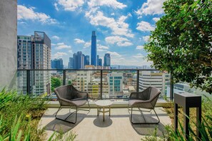 Un balcón con dos sillones de mimbre, una mesita y vistas a un paisaje urbano con edificios altos.