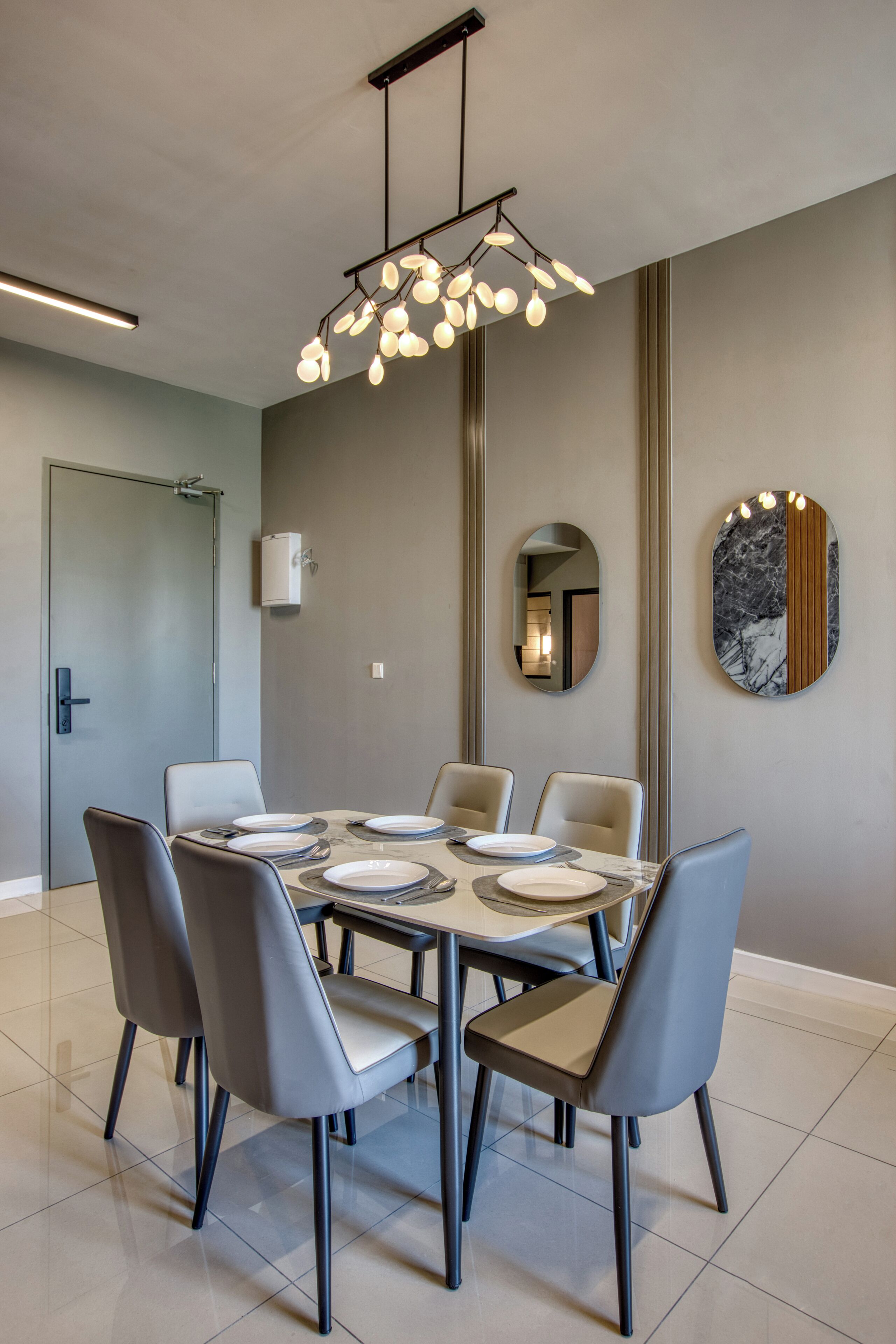 A modern dining area with a round table, six chairs, and a unique pendant light fixture.