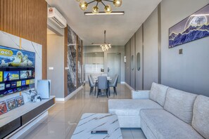 A modern living room with a flat-screen TV, a sofa, a dining area with a table and chairs, and a kitchen in the background. - High Floor KL Tower, PS5 With Games, Infinity Pool (Kuala Lumpur)
