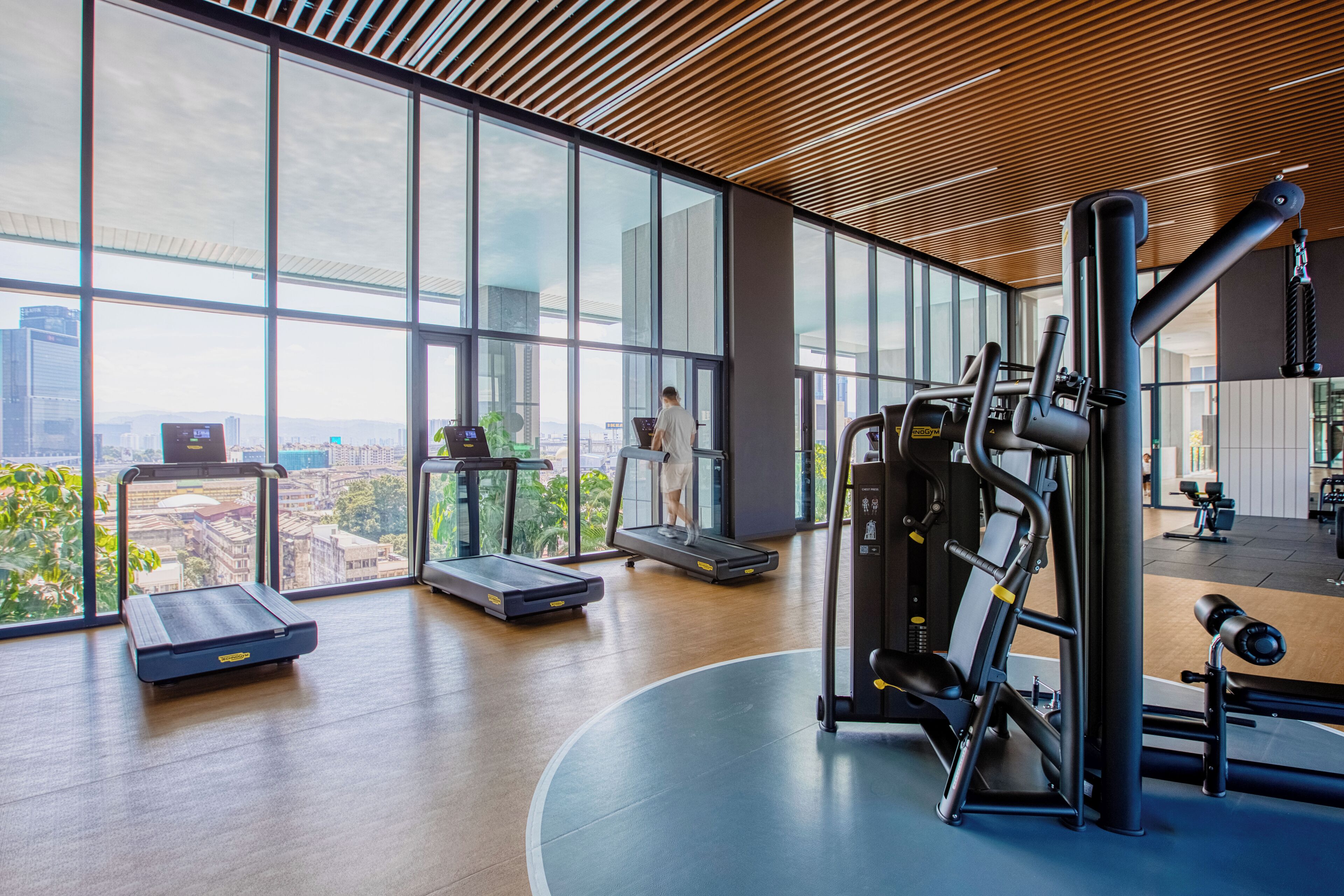 A gym with exercise equipment, large windows, and a city view.