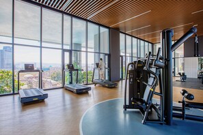 Un gimnasio con equipamiento de ejercicio, grandes ventanales y vistas a la ciudad.