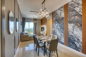 A modern dining area with a marble accent wall, a dining table set for four, and a city view through large windows. - High Floor KL Tower, PS5 With Games, Infinity Pool (Kuala Lumpur)