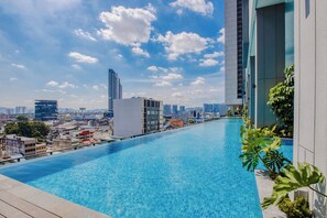 Piscina infinita no terraço com vista para o horizonte urbano, edifícios modernos e céu claro.