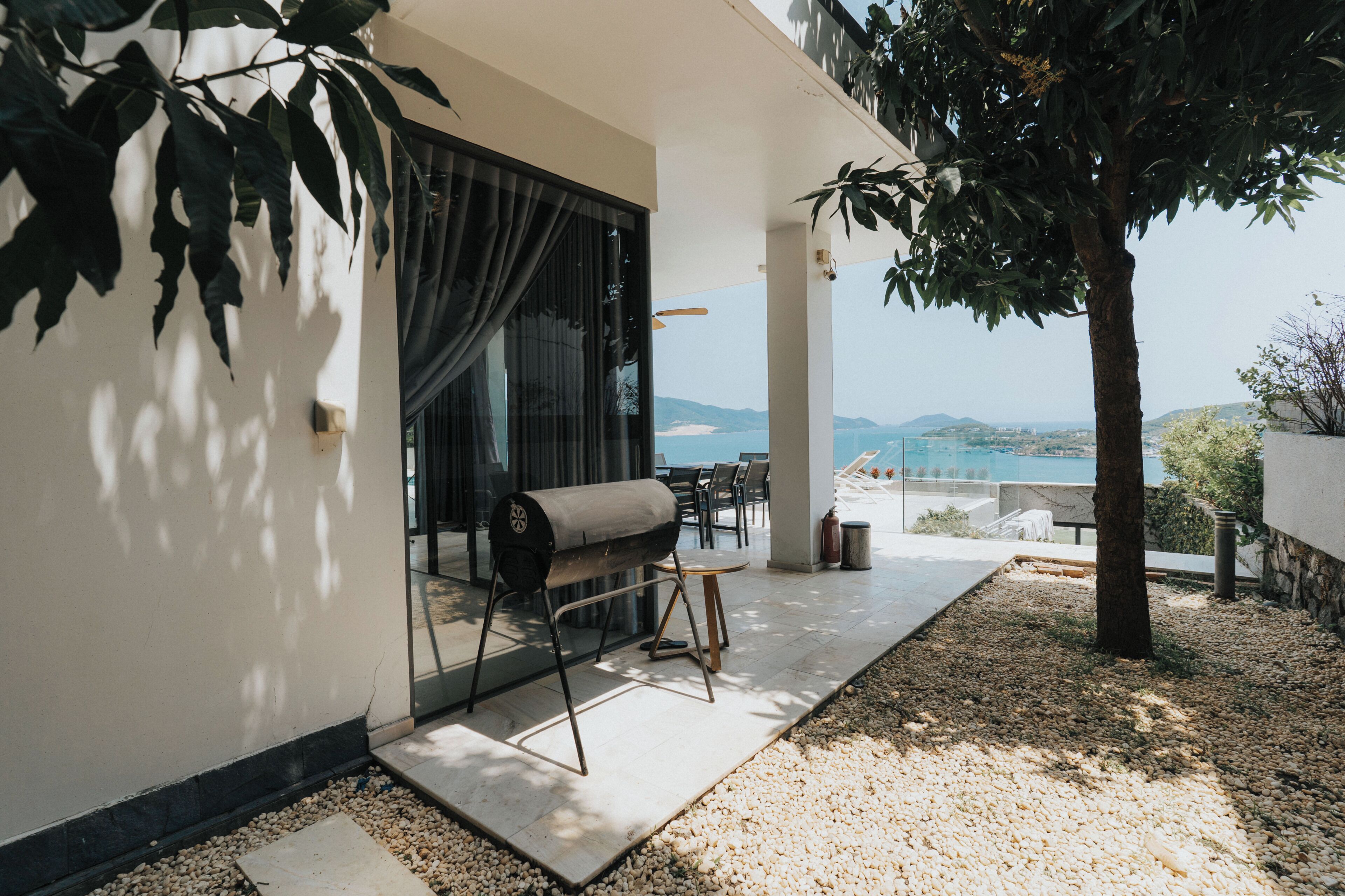 A modern outdoor seating area with a grill, a table, and chairs, overlooking a scenic view.