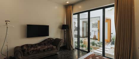 A hotel room with a sofa, a flat-screen TV, a bed, a large sliding glass door leading to an outdoor area, and a floor lamp.