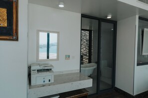 A bathroom with a glass shower enclosure, a toilet, and a sink with a paper towel dispenser.