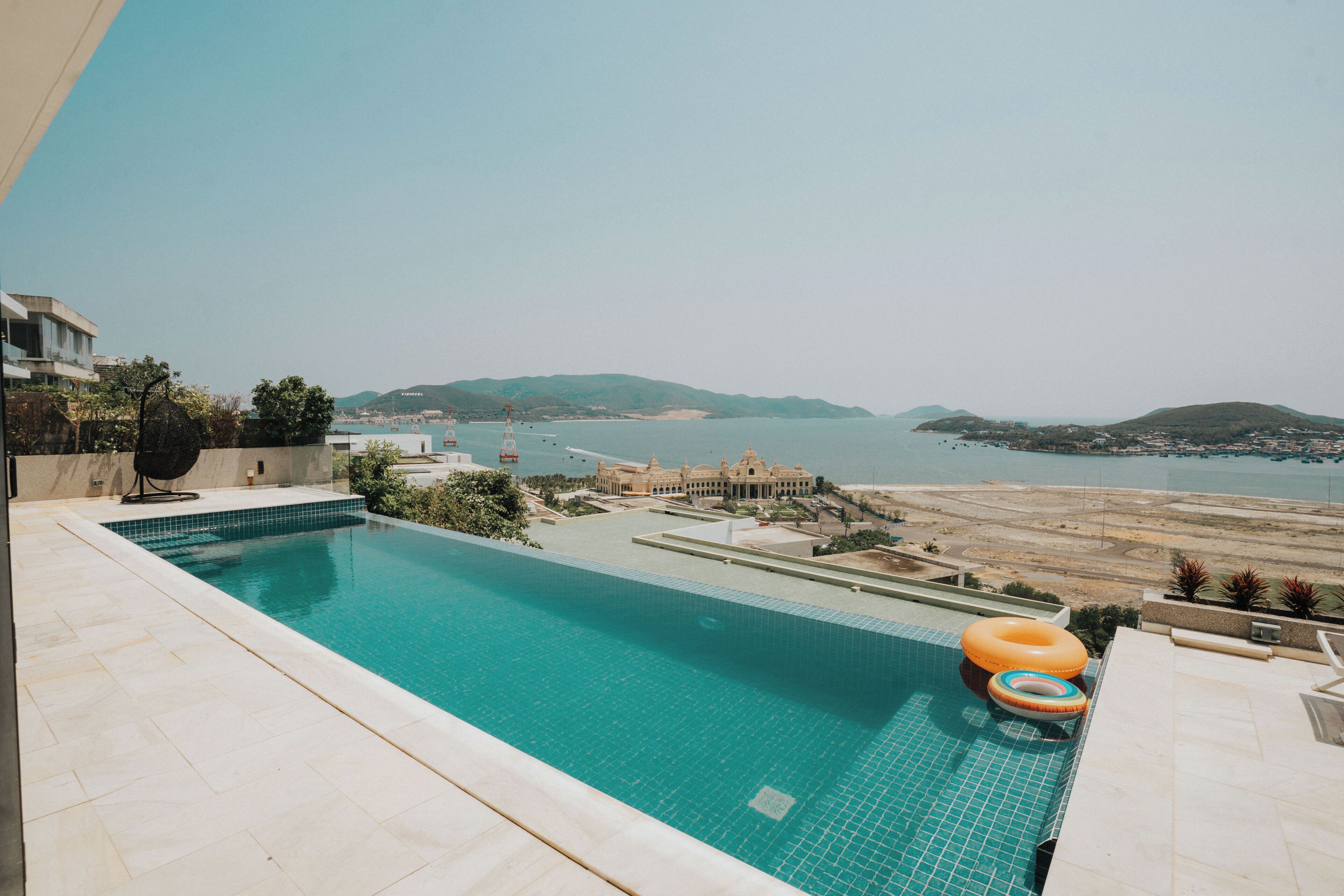 Une piscine offrant une vue sur une zone côtière, avec notamment un bâtiment à l’architecture caractérisée par des dômes et un paysage vallonné en arrière-plan.