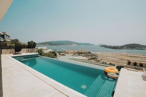 A swimming pool with a view of a coastal area, including a building with domed architecture and a hilly landscape in the distance.