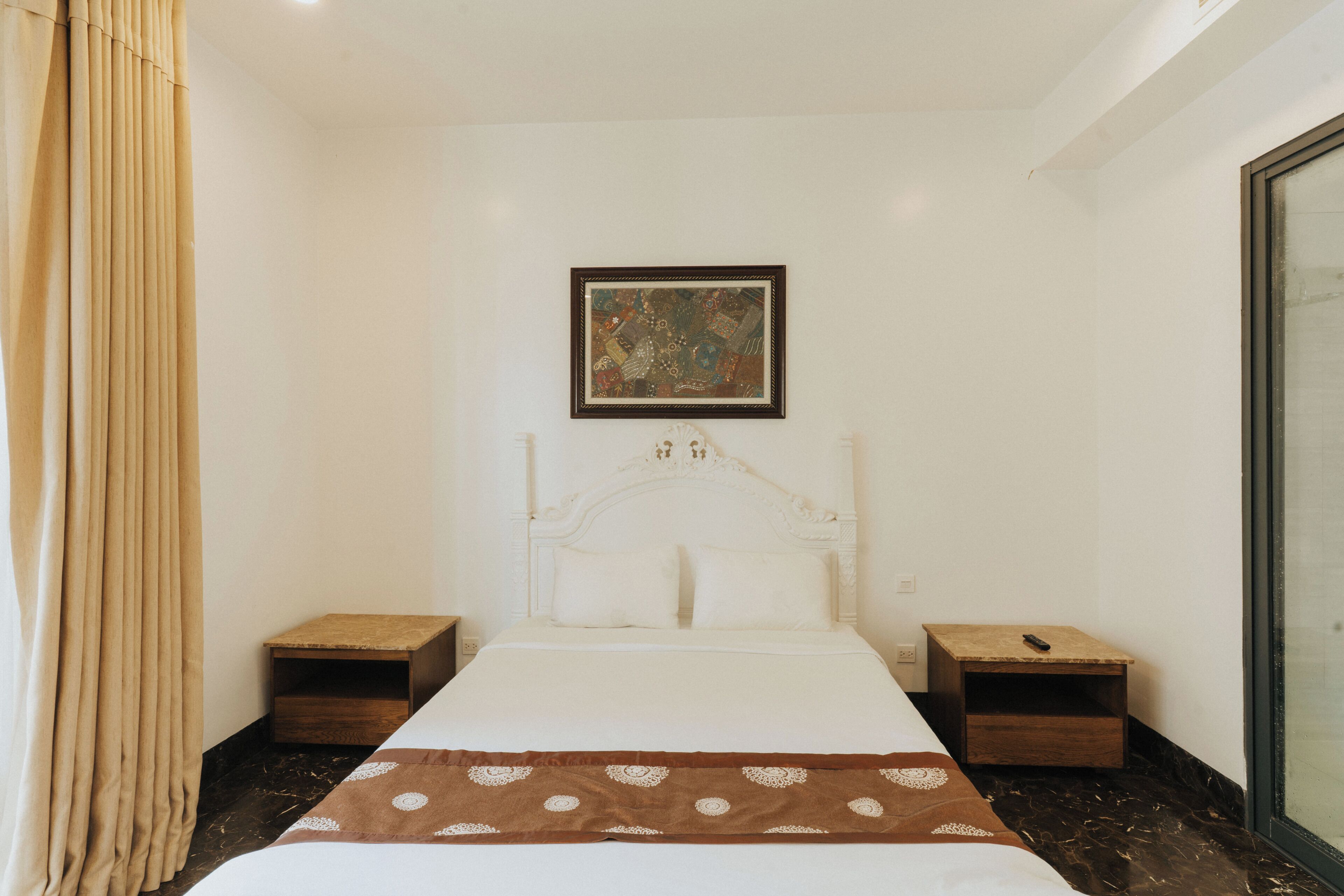 Une chambre d’hôtel avec un lit, deux tables de chevet, une commode, un tableau encadré au mur et une fenêtre.