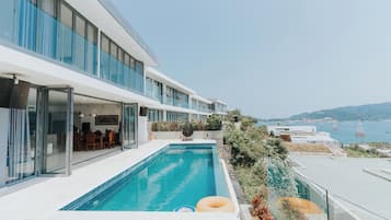 A modern hotel with a swimming pool, outdoor seating, and a view of the sea.