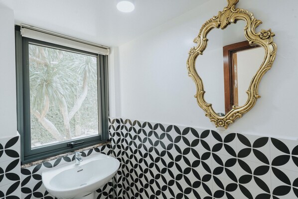 Un baño con un lavamanos blanco, un ventanal con vistas a palmeras y un espejo decorativo con un marco ornamentado.