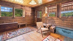 A log cabin interior with a wooden ceiling, a bench, a chair, a floor lamp, and a fireplace. - White Mountains Cabin w/ Pond & Scenic Deck (Lisbon)