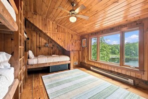 Una cabana amb un llit d'alt, un ventilador de sostre, una finestra gran amb vista al bosc i un paviment de fusta.