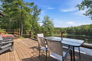 A wooden deck with outdoor furniture, overlooking a lake and forest. - White Mountains Cabin w/ Pond & Scenic Deck (Lisbon)