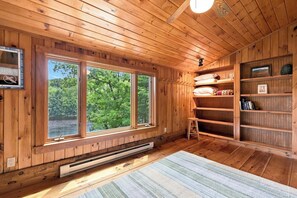 Interior de una cabaña de madera con ventanas amplias, una estantería empotrada y un calentador.
