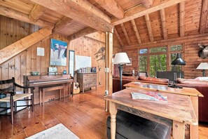Ein gemütliches Blockhaus-Interieur mit Holzbalkendecke, einem Klavier, einem Esstisch und einem Kamin.