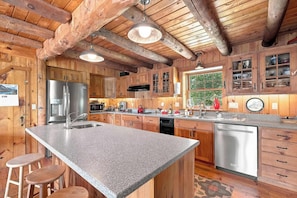 A kitchen with wooden cabinets, a granite countertop, stainless steel appliances, and a large window. - White Mountains Cabin w/ Pond & Scenic Deck (Lisbon)