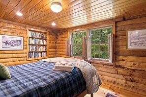 Ein Schlafzimmer in einer Blockhütte mit einem Bett, einem Bücherregal und einem Fenster mit Fensterläden.