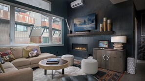 A modern living room with a sofa, coffee table, fireplace, and a large window overlooking a building. - Yampa Valley Views, Hot Tub + Wildhorse Gondola Access | Konik Chalet (Steamboat Springs)