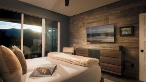 Quarto com uma cama grande, parede de madeira, televisão e porta de vidro deslizante para uma varanda.