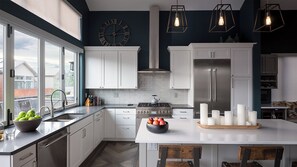 Une cuisine moderne avec des meubles blancs, un grand îlot central, une cuisinière à gaz et un réfrigérateur en acier inoxydable.