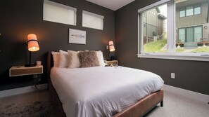 A bedroom with a large bed, two bedside tables, a window, and a view of a building outside. - Yampa Valley Views, Hot Tub + Wildhorse Gondola Access | Konik Chalet (Steamboat Springs)