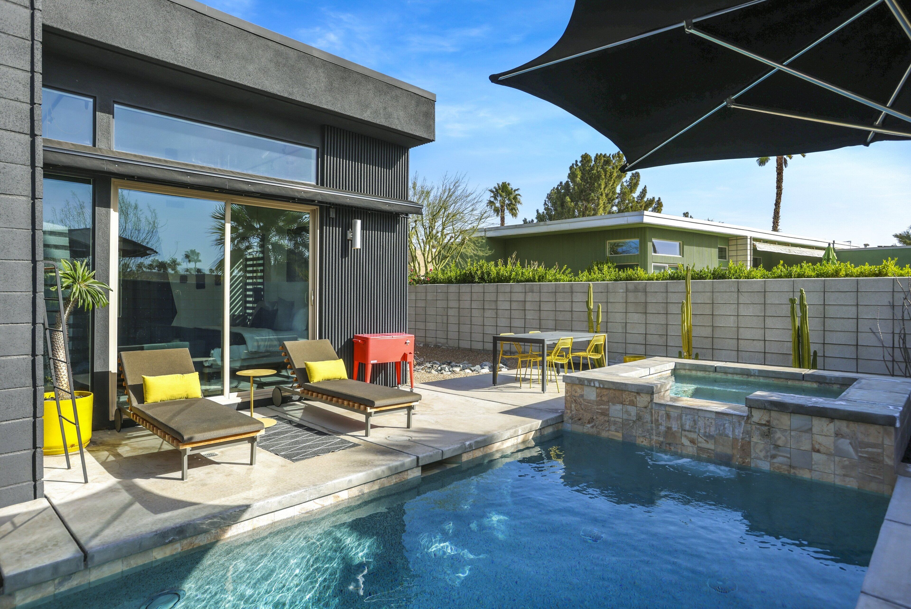 A modern outdoor pool area with lounge chairs, a hot tub, and a patio table.