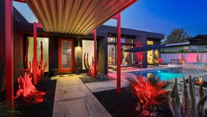 Una casa moderna con piscina, iluminación roja y un área de patio cubierta.