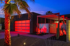 A modern building with a garage door illuminated in red, a covered patio area, and a palm tree. - Welcome to Casa Black - 3 Bedroom 3 Bathroom in the Palm Springs Area (Palm Springs)