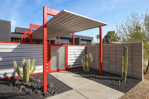 A modern building with a red and white color scheme, featuring a covered patio area with cacti and a concrete pathway. - Welcome to Casa Black - 3 Bedroom 3 Bathroom in the Palm Springs Area (Palm Springs)