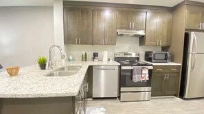 A modern kitchen with stainless steel appliances, a granite countertop, and wooden cabinets. - Cozy 2-Bedroom Peaceful Modern Home - Monthly Discount (Riverdale)